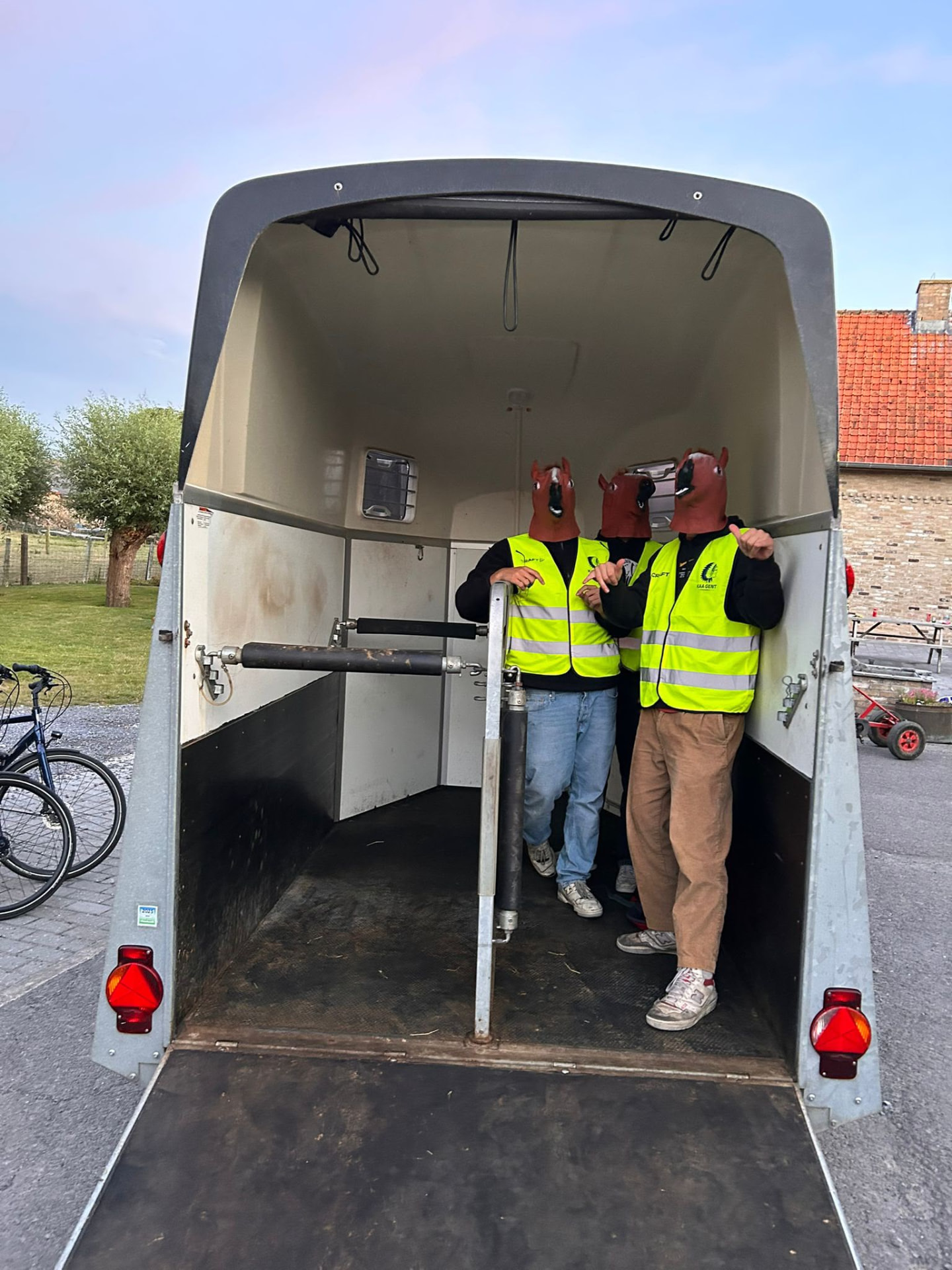 Drie helpers met paardenmaskers in een aanhangwagen